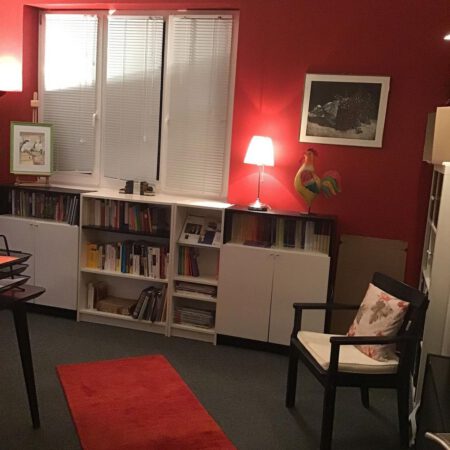 Ein Zimmer mit roter Wand, Bücherregal und Stuhl